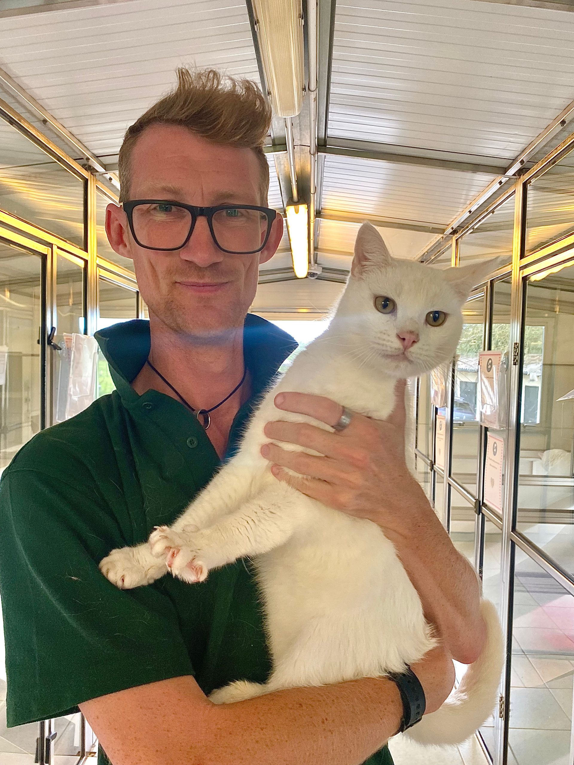 A person holding a white cat and smiling at the camera