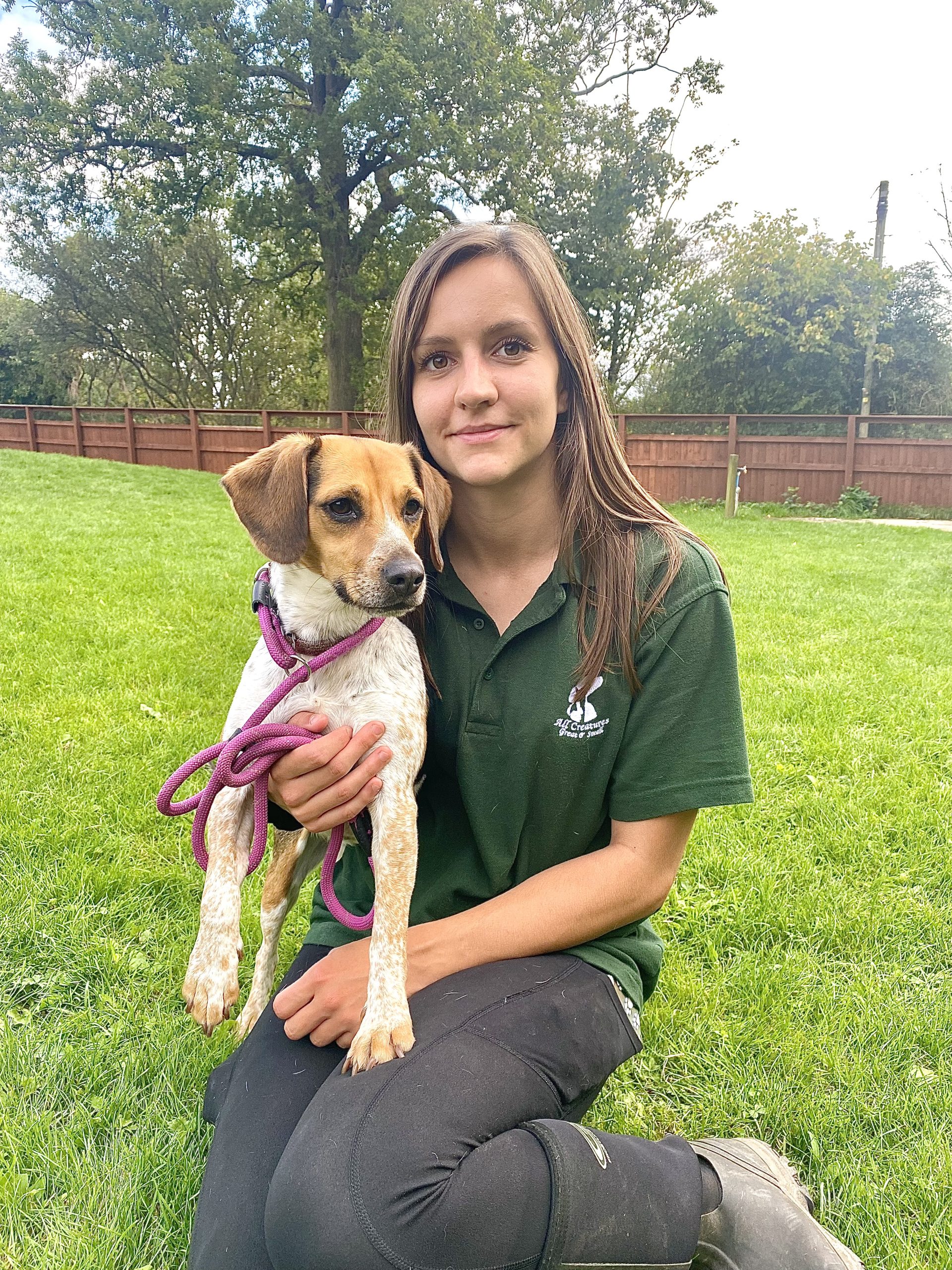 Staff member sitting on grass carrying a small dog.